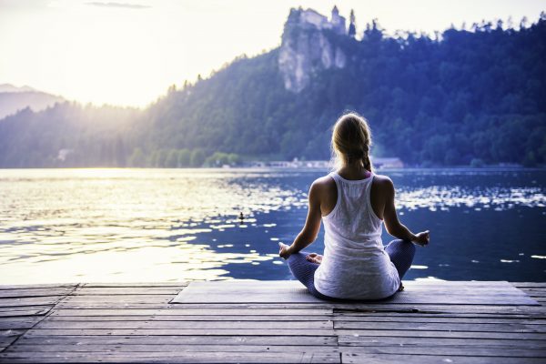 woman meditating on dock by lake